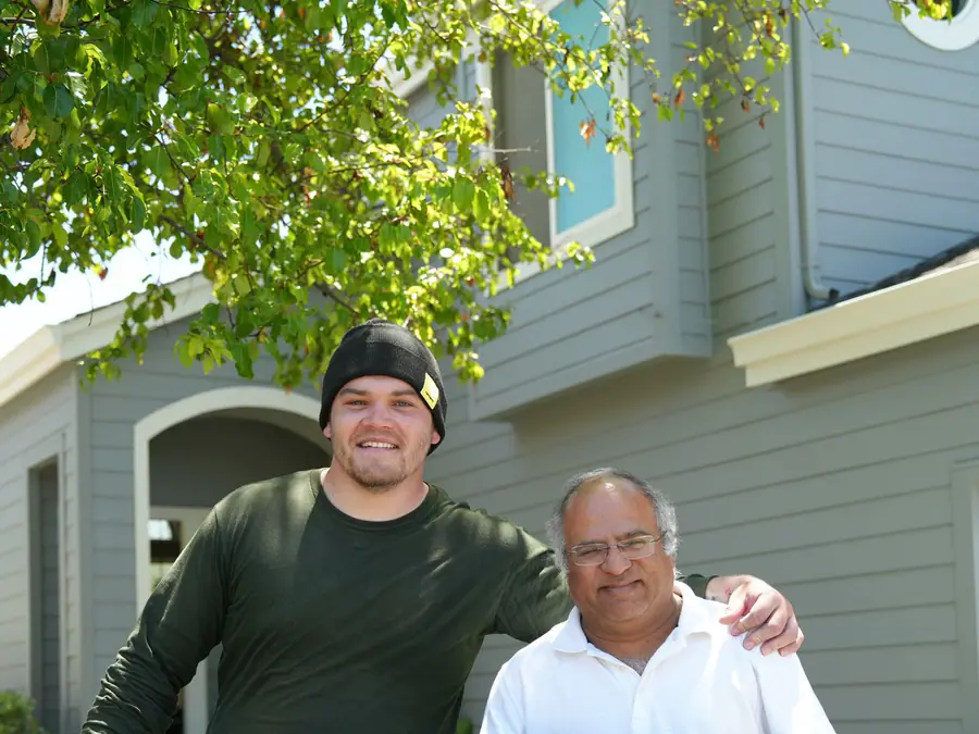 Smiling Hamilton crew member and homeowner holding a Hamilton yard sign in front of the finished home