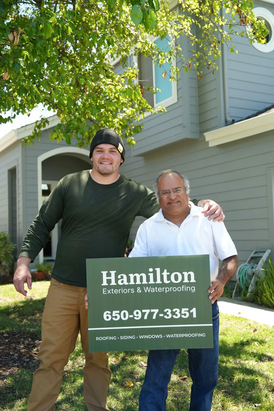 Two people holding a Hamilton Exteriors project sign